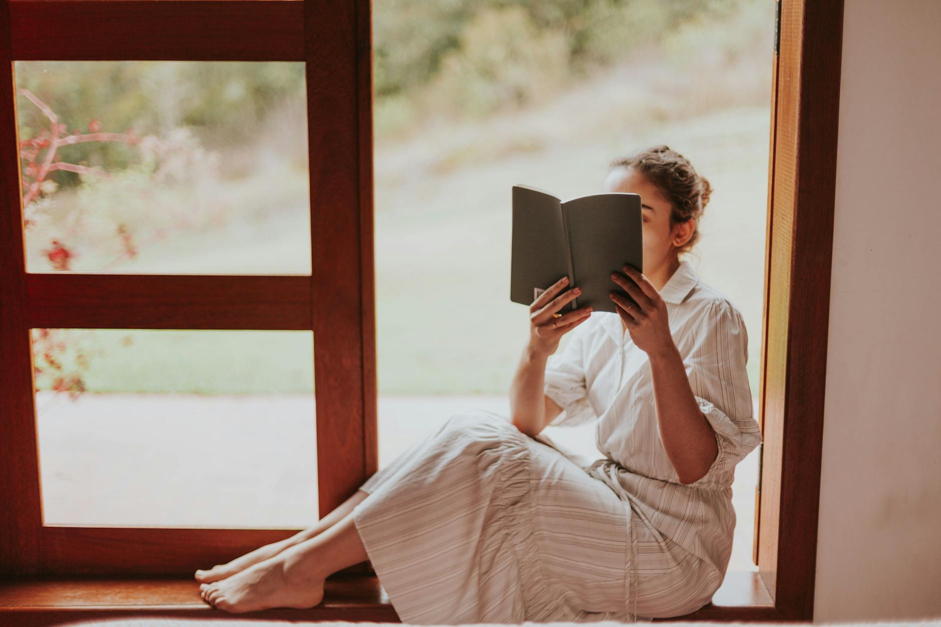 A a busy mom sitting by a window, relaxing and reading a book,