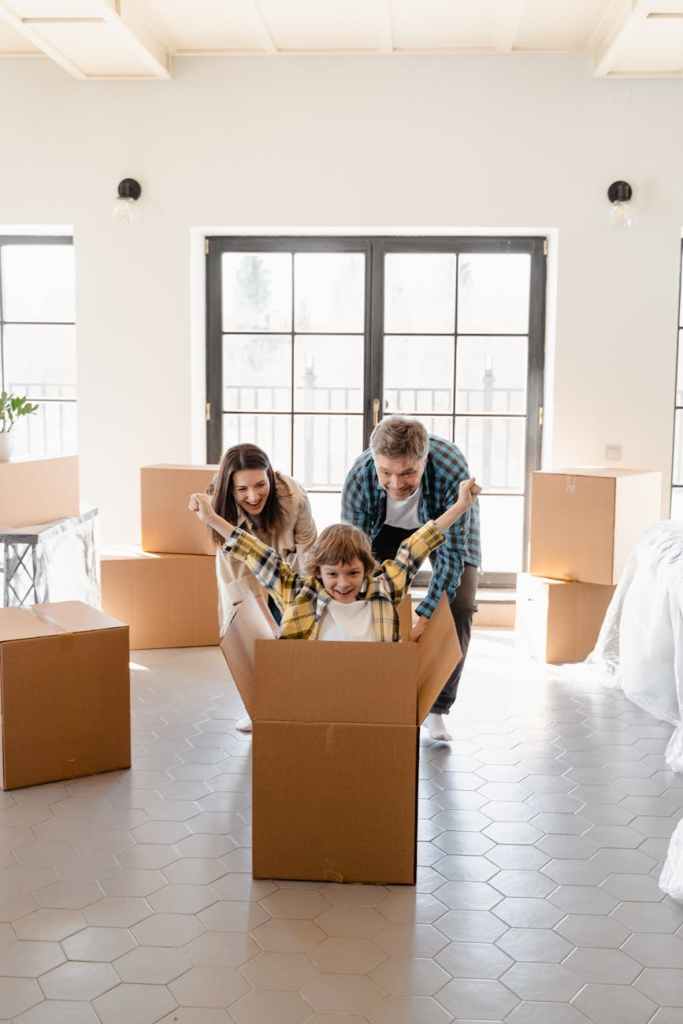 parents working together to pack up their house while having fun pushing their child in a moving box across the floor