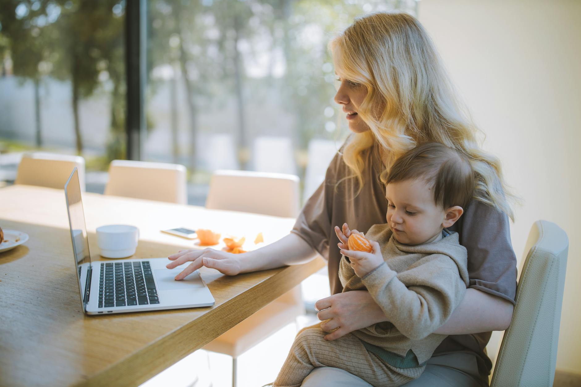 mom working on computer while her young child sits on her lap
