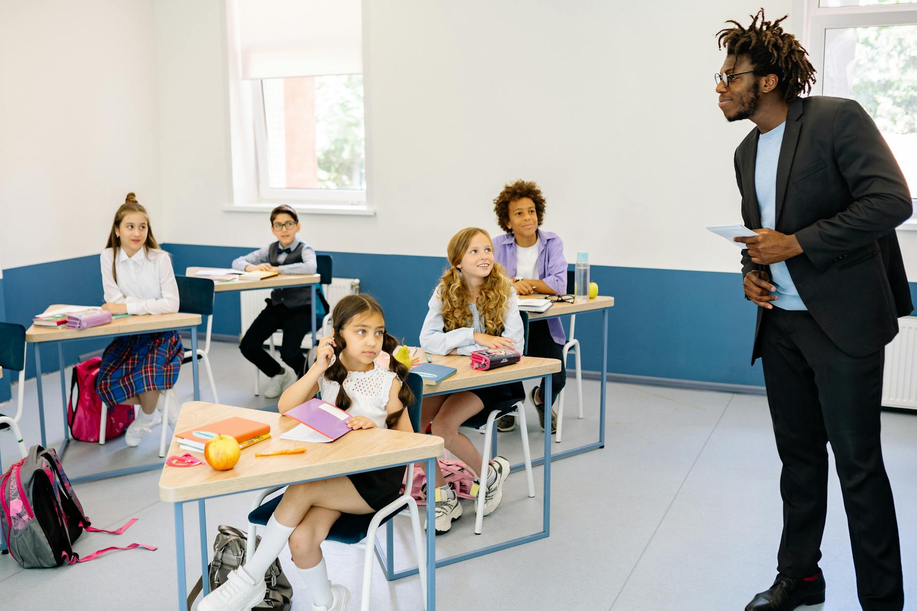 Five students sitting at their desk in a classroom listening and looking at their teacher