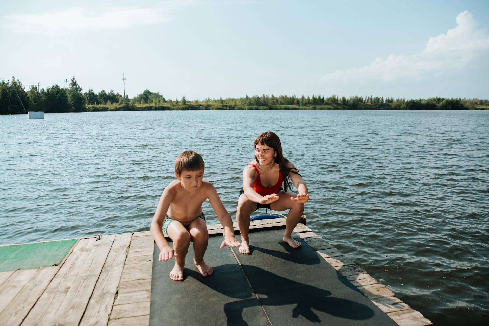 Mom and son on a dock by the lake doing squats. 