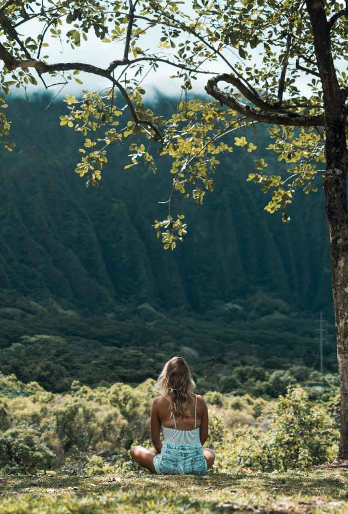 mom sitting on the ground mindfully looking at the forest around her. 
