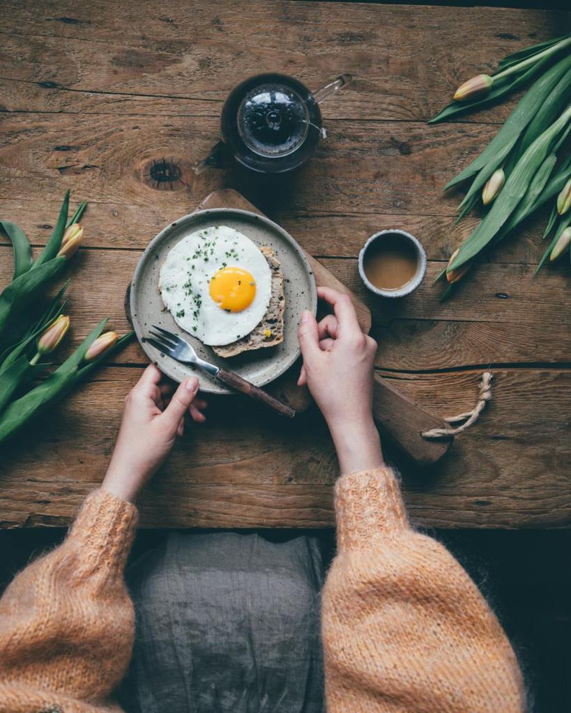Woman at breakfast table eating an egg and toast